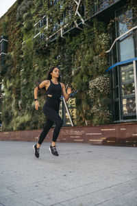 Side view of young female jogger running in a city with a garden facade building in the background