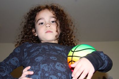 Low angle portrait of confident girl holding soccer ball against ceiling