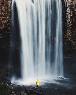 Person wearing yellow raincoat looking at majestic waterfall in forest