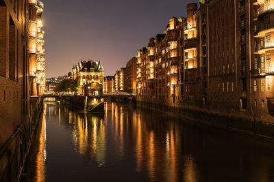 Canal amidst illuminated buildings in city at night