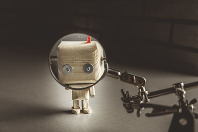 Wooden robot android stands on a table under a magnifying glass. metal clamps with magnifying glass