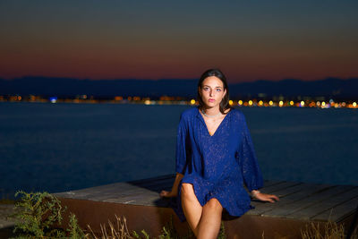 Portrait of young woman sitting against blue sky during sunset