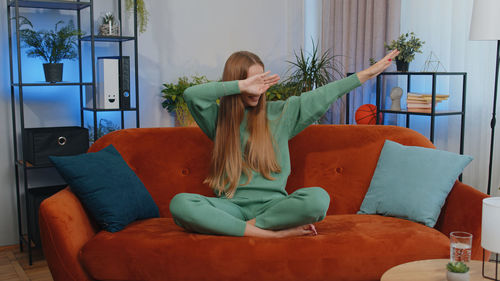 Rear view of woman using phone while sitting on sofa at home