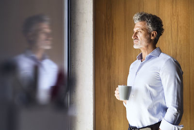 Reflection of mature businessman holding coffee mug