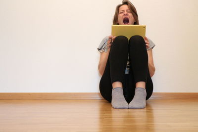 Portrait of young woman sitting on hardwood floor against wall