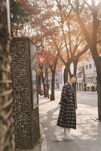 Woman standing by tree on street in city