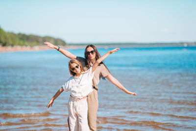 Woman with arms raised on beach against sky