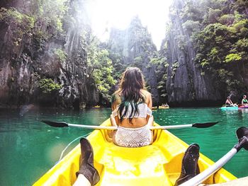 Rear view of women sitting on rock against water