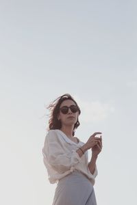 Low angle view of young woman looking away against sky