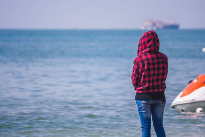 Rear view of young woman standing at beach on sunny day