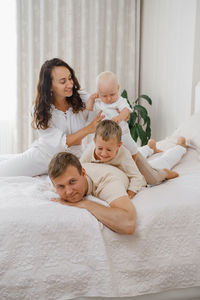 Family with two kids on the bed having fun. mather, father baby and toddler sons are happy in the