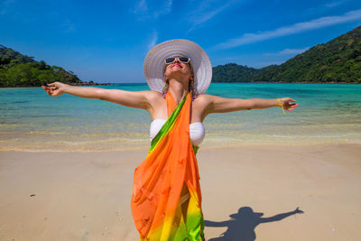 Woman standing with arms outstretched at beach against sky