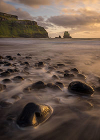 Rocks on beach against sky during sunset