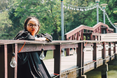 Portrait of woman standing by railing against trees