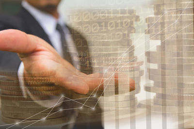 Digital composite image of businessman pointing towards coins by graphs in office