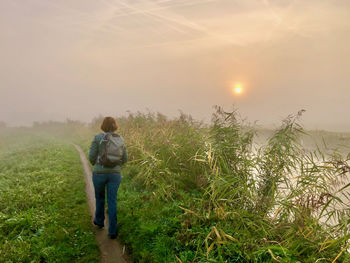 Rear view of woman walking along a misty canal with the sun just coming through