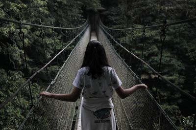 Rear view of woman standing on footbridge in forest