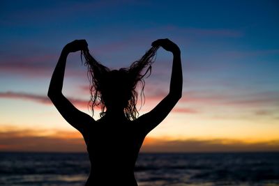 Silhouette woman holding hair at beach against sky during sunset