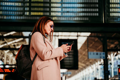 Woman using mobile phone while standing at railroad station