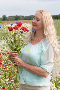 Beautiful middle-aged blonde woman stands among a flowering field of poppies