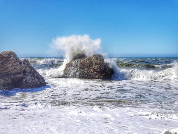 Sea waves splashing on shore against clear blue sky