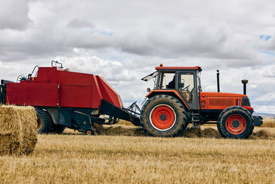 Dried hay roll and modern tractor placed on agricultural field in mountainous area in summer