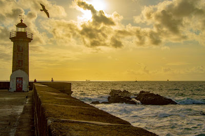 Lighthouse by sea against sky during sunset