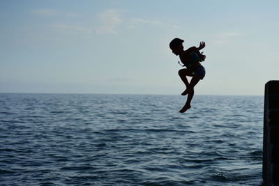 Full length of boy jumping in sea against sky