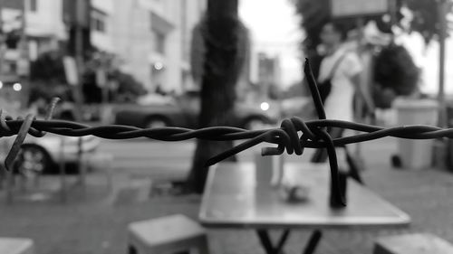 Close-up of barbed wire on street against fence