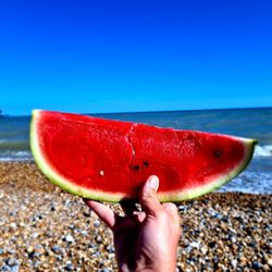 Midsection of man holding strawberry at beach against sky