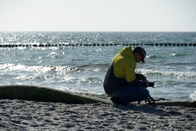 Man crouching while setting up camera at beach