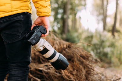 Midsection of man holding camera in forest