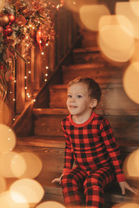 Portrait of cute girl sitting on illuminated christmas tree