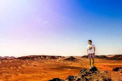 Full length of man standing on rock in desert against clear sky