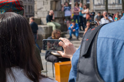 Rear view of woman photographing people at street