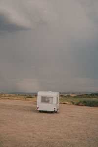 Motorhome parked on sandy terrain against rock cloudy sky in daytime