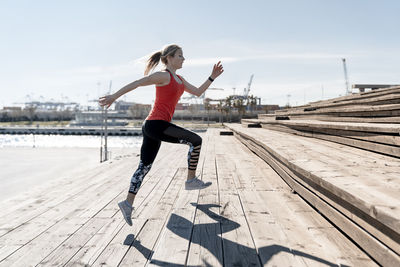 Female jogger doing warm up exercise on steps during sunny day