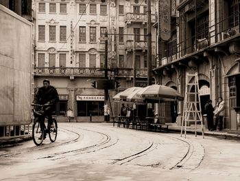 Rear view of man riding bicycle on street against buildings