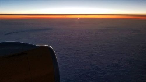 Airplane flying over sea against sky during sunset