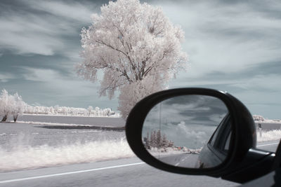 Close-up of side-view mirror against sky