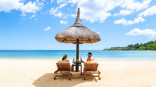 Rear view of woman sitting on beach against sky