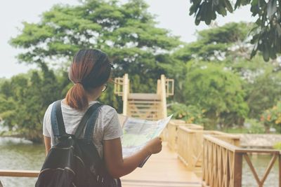 Rear view of woman standing by railing against trees