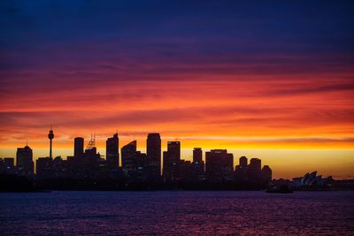 Silhouette of city at waterfront during sunset