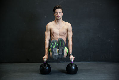 Portrait of shirtless man exercising with kettlebells in gym