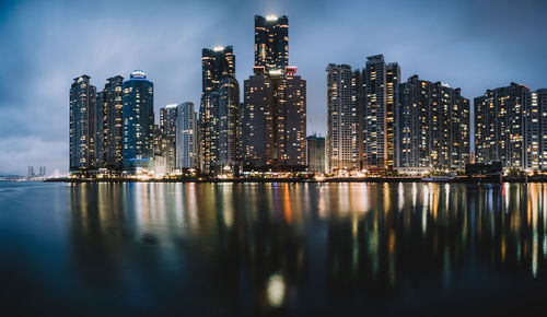 Illuminated buildings by river against sky at night