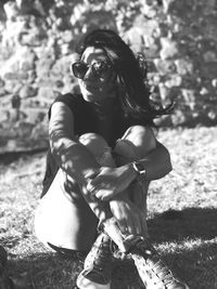 Woman wearing sunglasses while sitting on field during sunny day