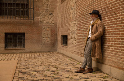 Portrait of adult man in hat and coat against wall on street