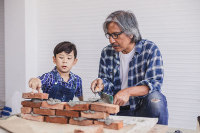 Mature man assisting boy in making brick wall at workshop