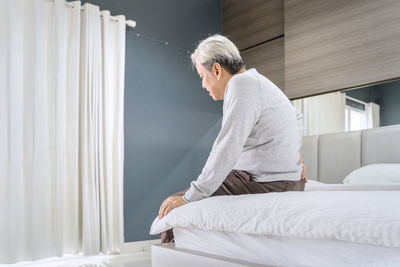 Side view of man sitting on bed