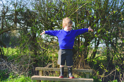 Boy standing by plants against trees